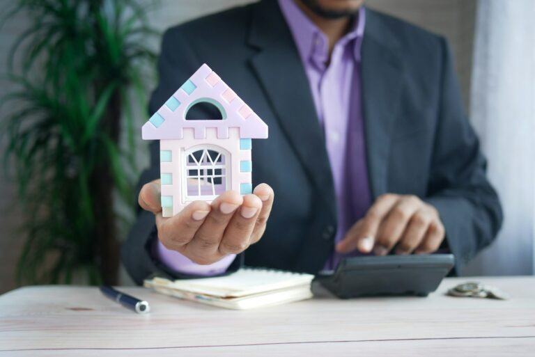 man holding model house at desk with calculator; CLO ratings providers