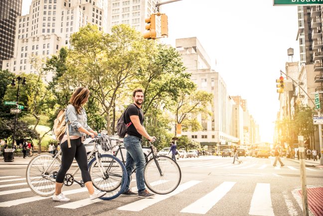 Two people walking their bikes on crosswalk in New York City