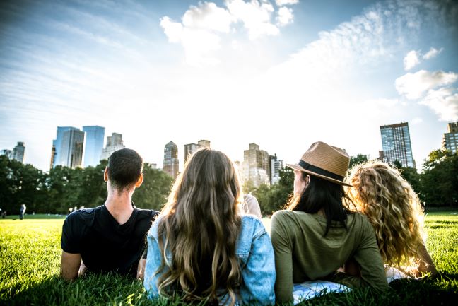 Group of friends laying in the grass together in Central Park facing the city