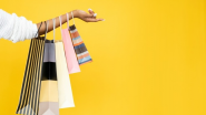 A woman's arm holding out shopping bags, against a yellow background.