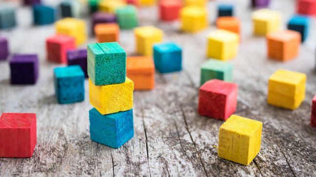 Wooden blocks of different colors scattered across a wooden floor, with a few blocks stacked on top of one another.