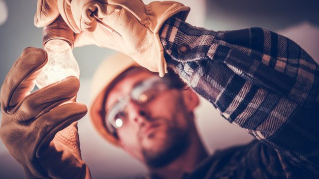 A close-up view of an electrician's hands fixing a lightbulb, with his face blurred in the background.