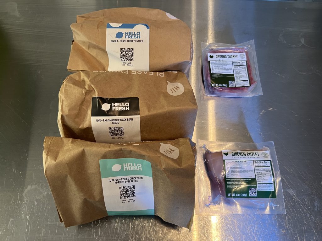 Three HelloFresh meal kits in paper bags with chicken and turkey on the side