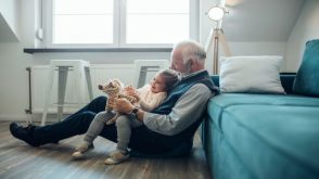 Grandfather sits on floor with grandchild on lap