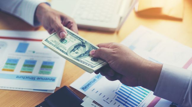 two men in a cash transaction over documents discussing revenue structure