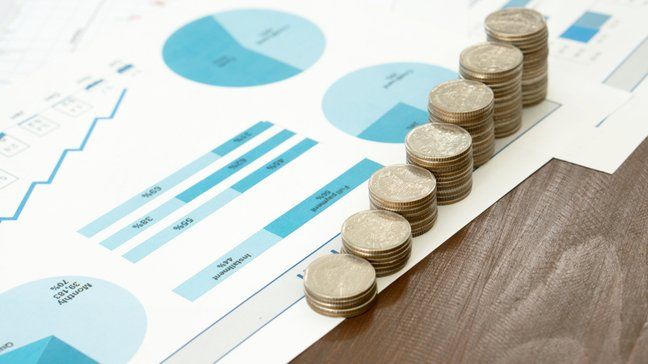 stacked coins over documents with pie charts and other figures on investing returns