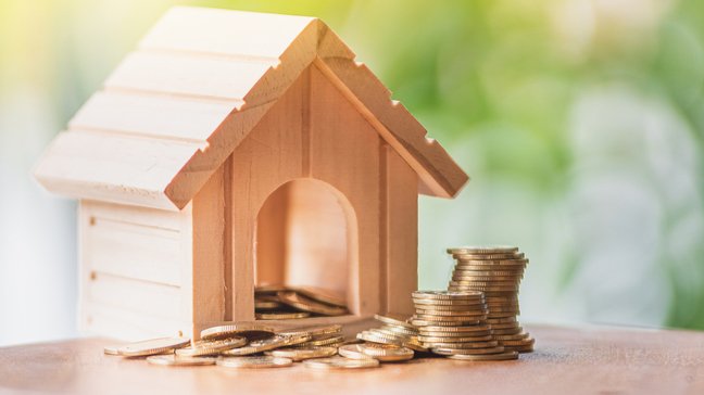 A Beginner’s Guide To Mortgage Loans: A small wooden model house overflowing with coins.