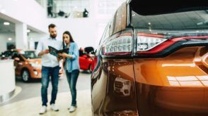 A couple in a car dealership, looking at a binder, next to a car