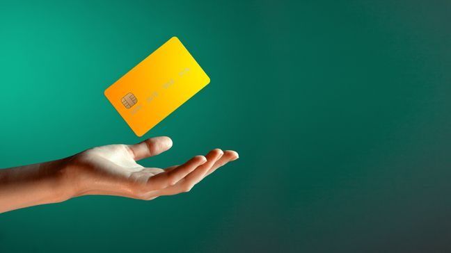 A hand tossing a credit card in the air, in front of a green background