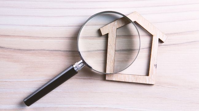 A magnifying glass overtop of a wooden outline of a house