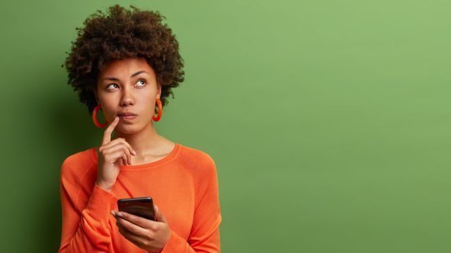 Young woman holding a phone and looking up questioningly