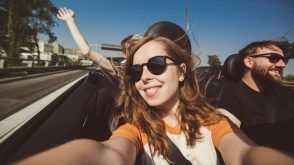 Young adults driving on the highway in a convertible, with hands in the air
