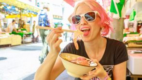 Young woman in sunglasses eating with chopsticks from a bowl