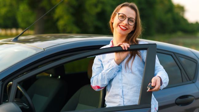 Young woman holding the driver door of a car open