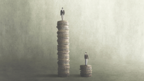 One man standing on a tall stack of coins; another standing on a considerably smaller stack