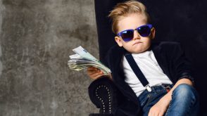 Young child in sunglasses, leaning in a chair and holding a stack of dollar bills