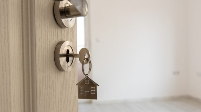 A house keychain dangling from a key in a door lock