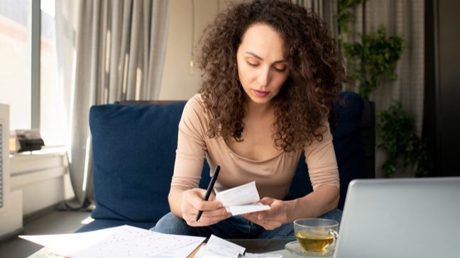 Young woman looking at paper bills in front of a laptop