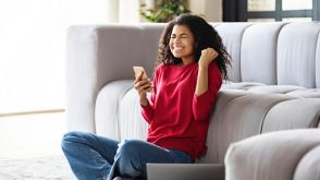 Woman celebrates while holding her phone and laptop