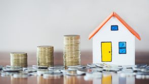 housing_market_expensive A toy house with a growing stack of coins beside it