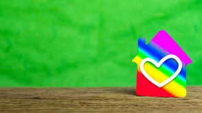 A rainbow-coloured toy house with a heart on it, in front of a green background