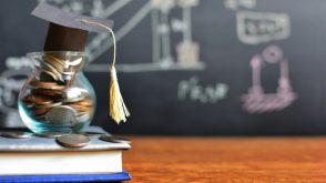 student_loans_coins_grad_cap A jar of coins on top of a stack of books, with a graduation cap perched on top.