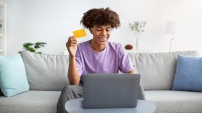 Teenager sitting on a couch, in front of a laptop and holding a credit card