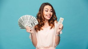 Young woman holding dollar bills fanned out in one hand and a credit card in the other hand.
