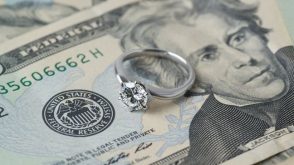 A diamond engagement ring sitting on top of American bills.