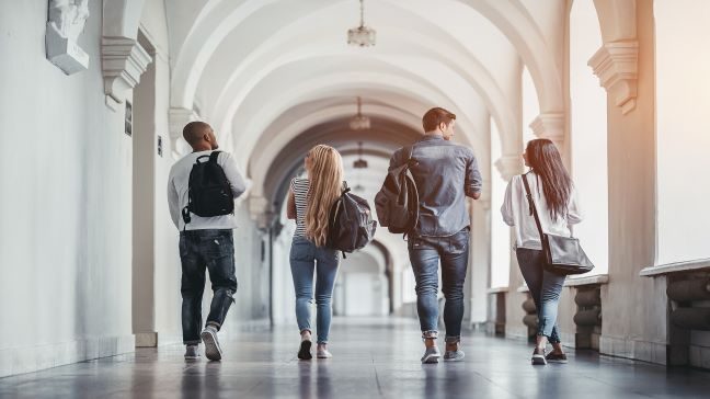Four college students walking down a corridor on a college campus talking to each other