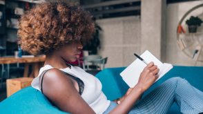 woman_journaling A young Black woman reclining on a couch and writing in a journal.