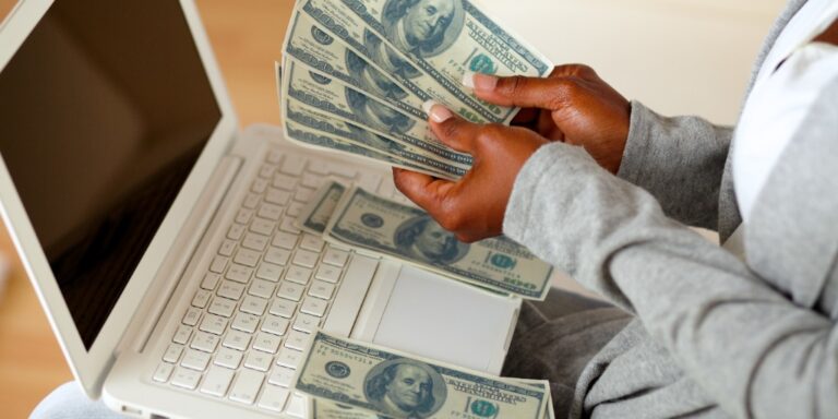 woman counting hundred dollar bills on laptop. From "How to make money online: 20 ideas for online income".