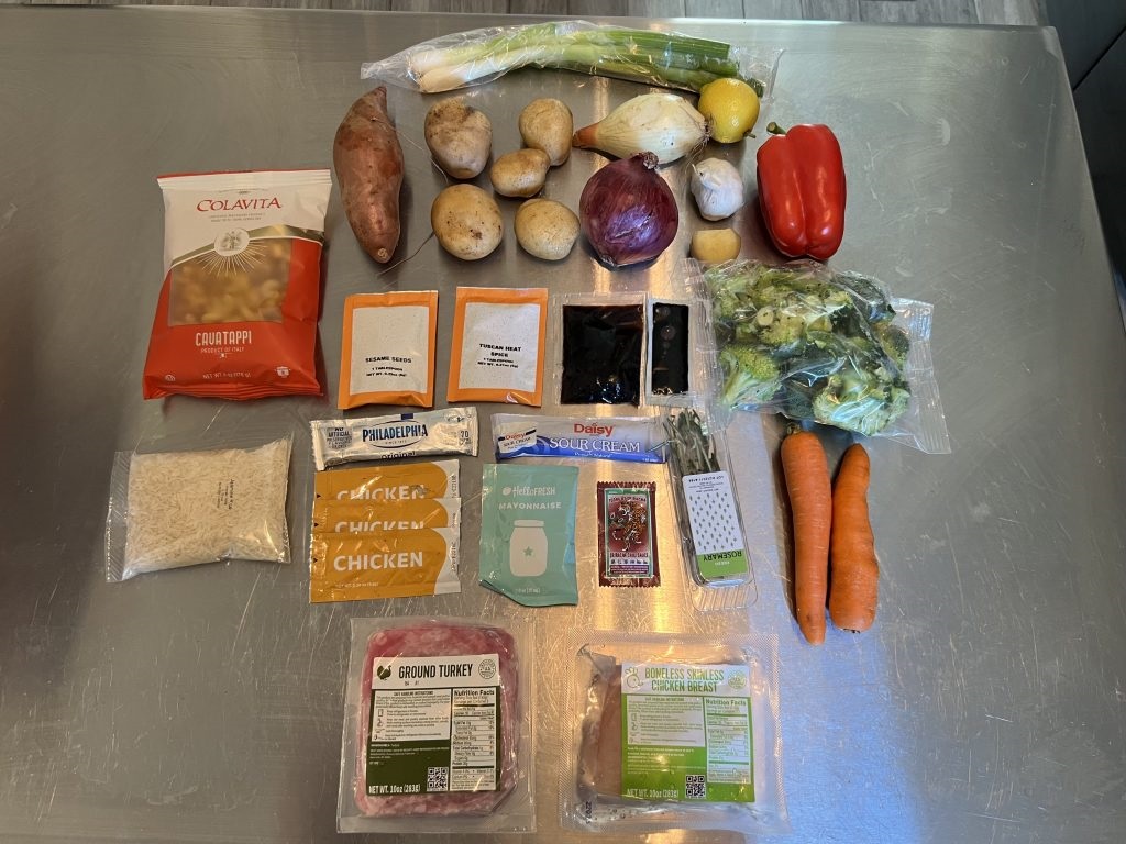 Ingredients received from EveryPlate to make lemon herb turkey cavatappi in a cream sauce spread out over kitchen island including scallions, including ground turkey, carrots and onions.