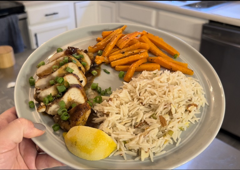 prepared turkish-spiced chicken dish with carrots and rice from HelloFresh held held by reviewer on blue plate