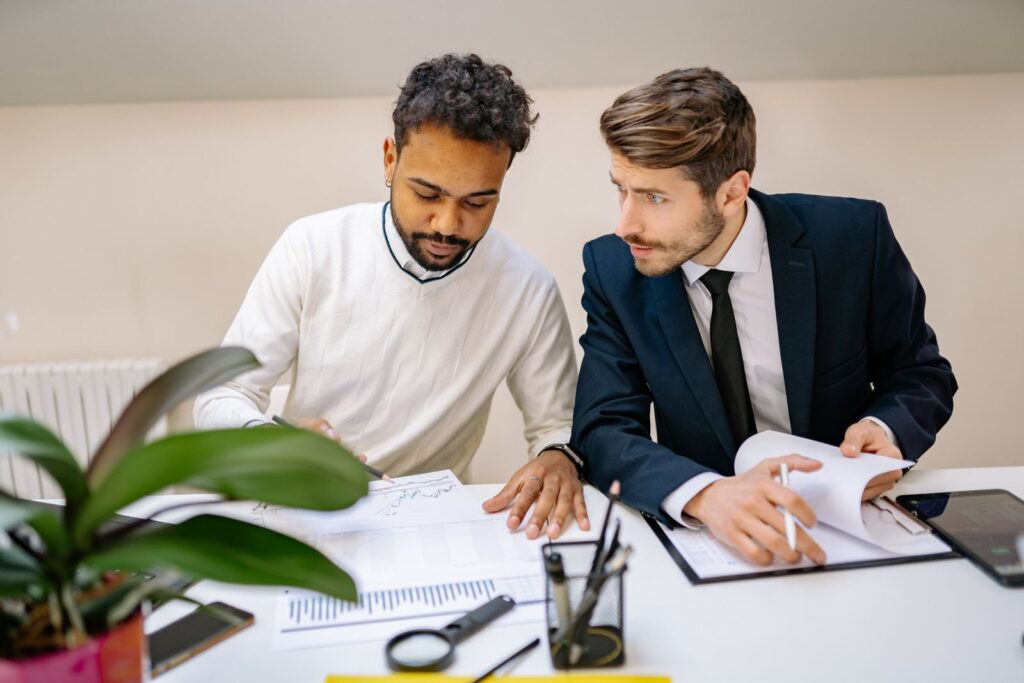 Two men in a modern office discussing and analyzing documents with charts.; buy a small business
