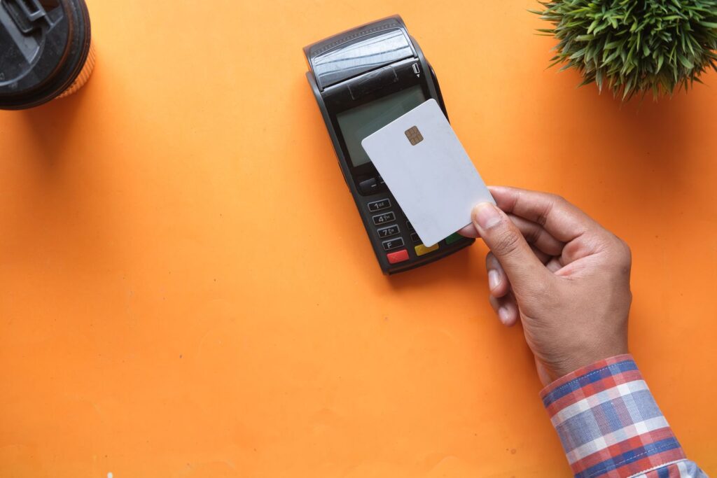 A person making a contactless payment with a credit card and card reader on a bright orange surface.; credit card interest rate cap