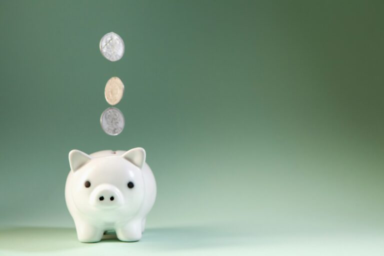 Coins falling into a white piggy bank.; financial loss