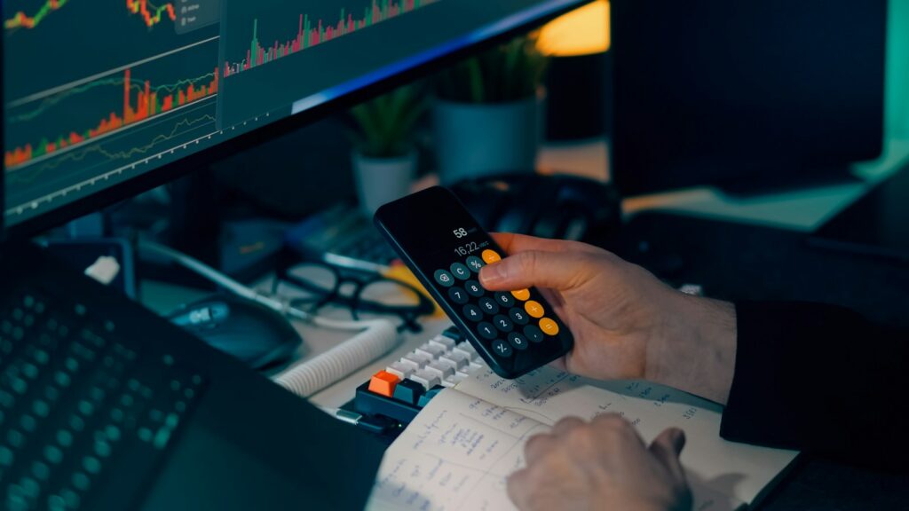 Person using calculator at desk with computer charts; build a financial plan