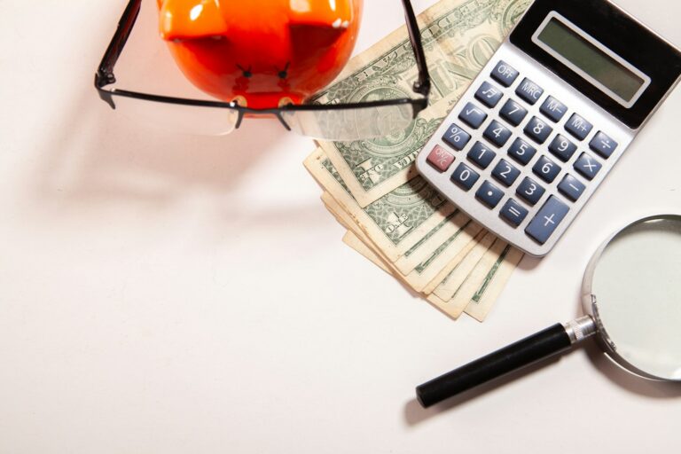 Calculator, magnifying glass, glasses, and money on white surface; saving and investing