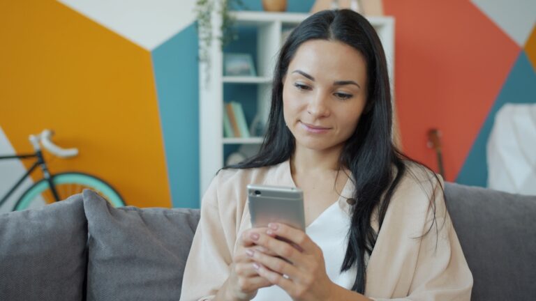 A woman looking at her smartphone on a couch.; reduce screen time