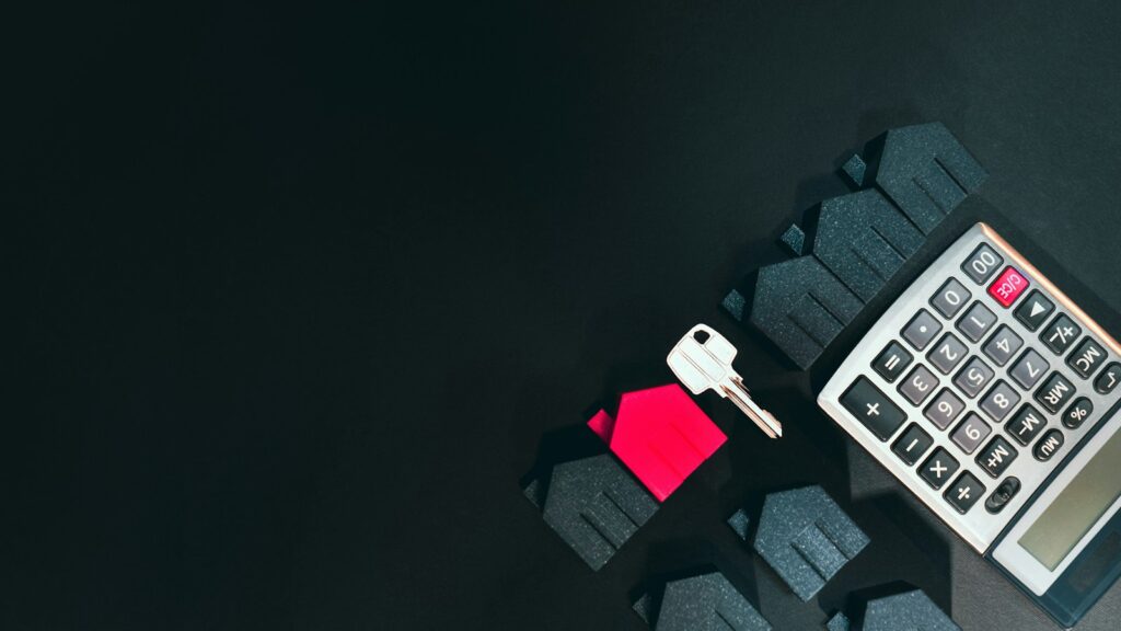 A silver key, a red house model, and a calculator on a black surface