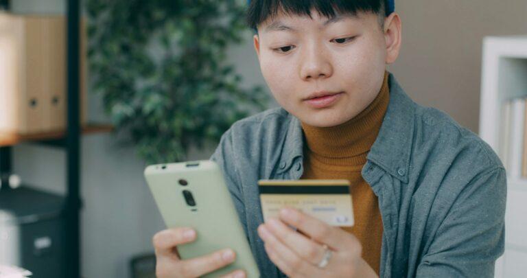 A man sitting at a table looking at a cell phone; student loan autopay discount