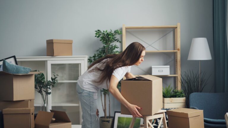 a woman moving boxes in a living room; job relocation costs
